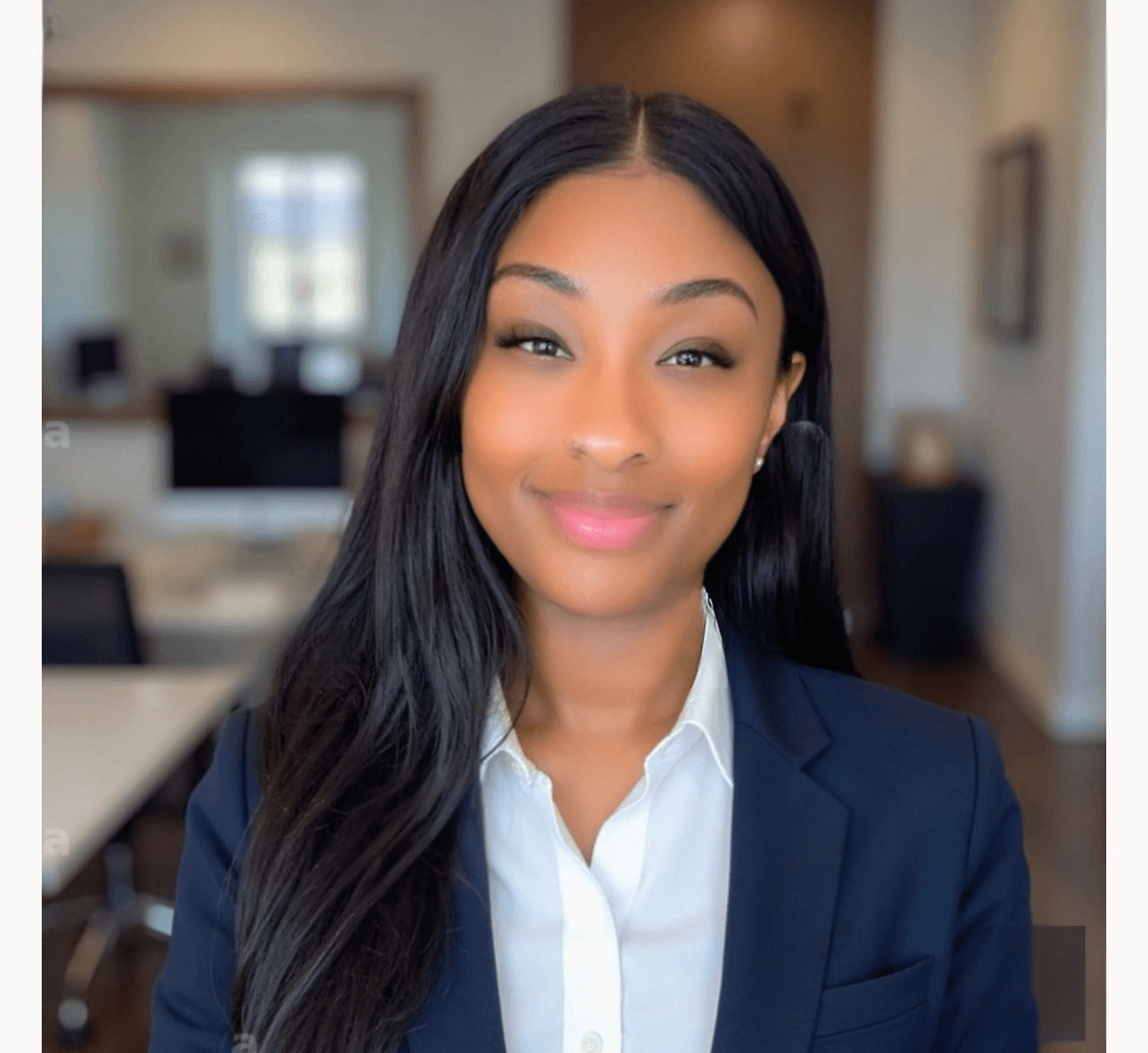 Smiling Black woman with long dark hair wearing a navy blazer and white collared shirt.
